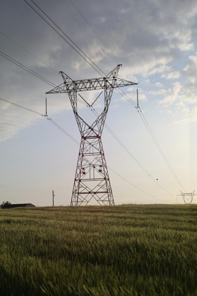 High voltage power line tower standing tall in a green field under a cloudy sky.
