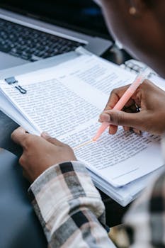 A person reviews documents and highlights important information at a desk with a laptop.