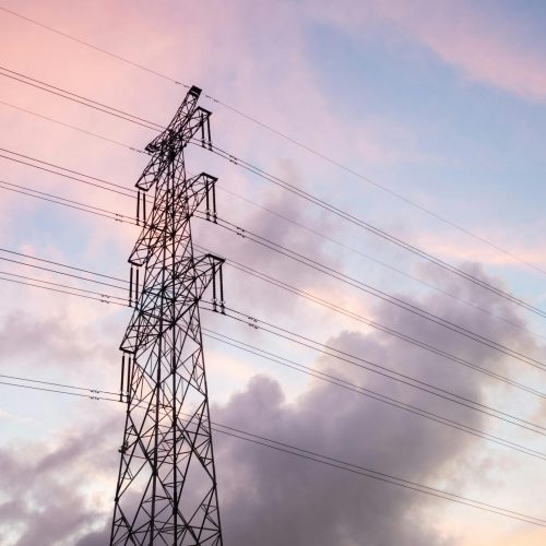 High voltage power lines silhouetted against a vivid sunset sky with clouds.