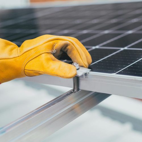 Close-up of a worker's hand with protective gloves adjusting a bolt on a solar panel.